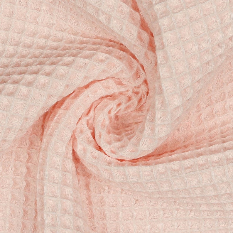 May include: A close-up of a soft, pink waffle weave fabric. The fabric is textured and has a subtle sheen.