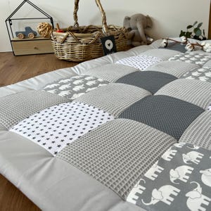 a cozy and inviting baby bedding set, including a gray and white quilt with elephant patterns, a woven basket, and a stuffed elephant toy.