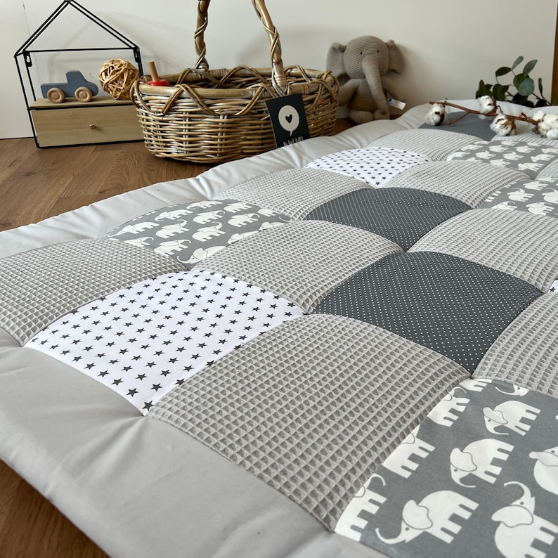 a cozy and inviting baby bedding set, including a gray and white quilt with elephant patterns, a woven basket, and a stuffed elephant toy.