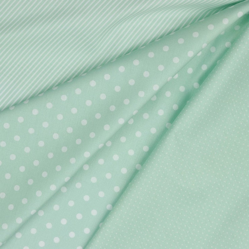May include: Three pieces of fabric in different patterns. The top piece is a light green fabric with white stripes. The middle piece is a light green fabric with white polka dots. The bottom piece is a light green fabric with a small white dot pattern.