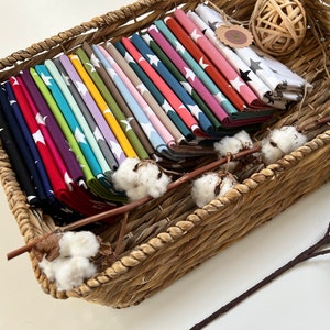 May include: A wicker basket filled with fabric squares featuring white stars on a variety of colored backgrounds. The fabric squares are folded and stacked neatly in the basket.