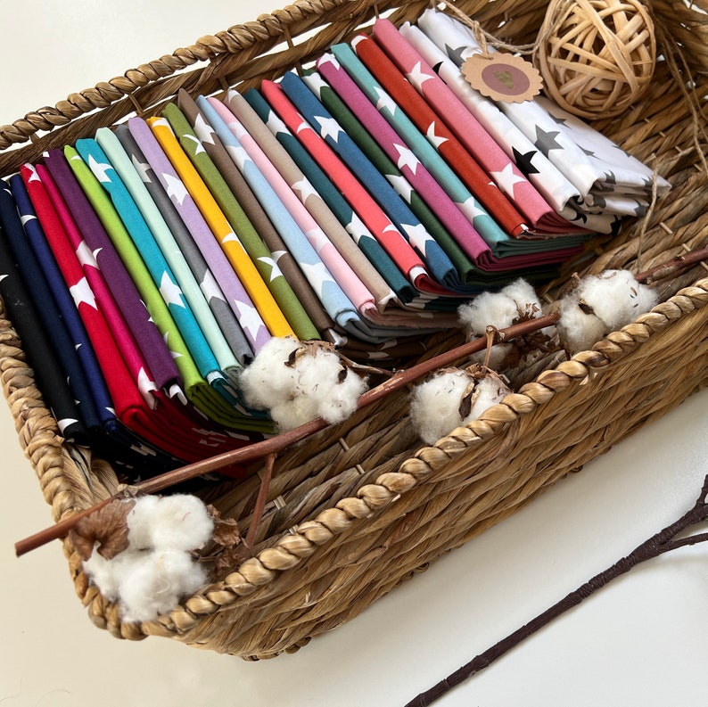 May include: A wicker basket filled with fabric squares featuring white stars on a variety of colored backgrounds. The fabric squares are folded and stacked neatly in the basket.