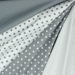 May include: An assortment of fabric swatches in various shades of gray and white, each adorned with a polka dot pattern. The fabric is draped, showcasing the different dot sizes and fabric textures.