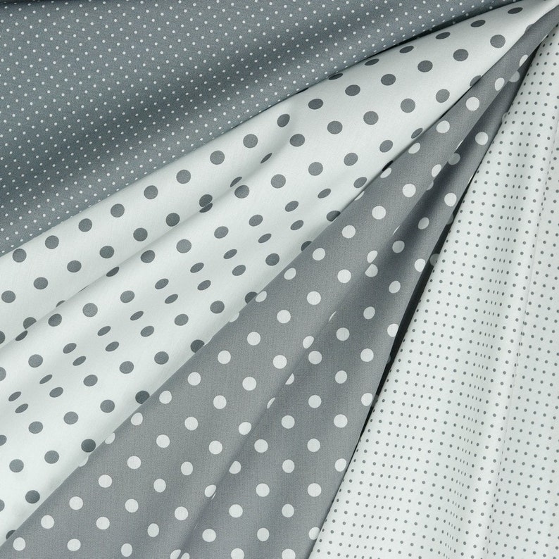 May include: An assortment of fabric swatches in various shades of gray and white, each adorned with a polka dot pattern. The fabric is draped, showcasing the different dot sizes and fabric textures.