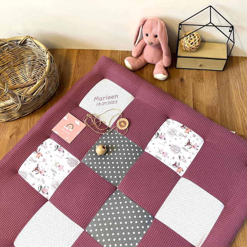 a pink stuffed rabbit, a woven basket, a wooden box, and a quilt with a pattern of gray and white polka dots.