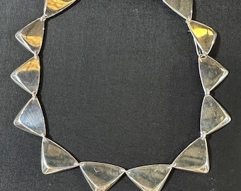 May include: A silver necklace with triangular links. The necklace is made of polished silver and has a simple, modern design.