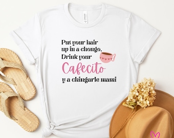 May include: White t-shirt with black text that reads "Put your hair up in a chongo, Drink your Cafecito y a chingarle mami". A pink coffee cup with hearts is next to the text.