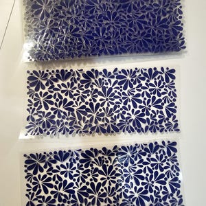 May include: Three clear plastic sheets with a repeating pattern of navy blue floral designs. The floral pattern is composed of stylized flowers and teardrop shapes. The sheets are stacked on a white surface.