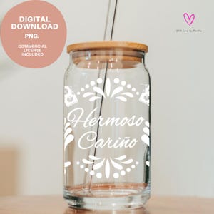 Peut inclure: Un gobelet en verre transparent avec un couvercle en bois et une paille en verre. Le gobelet présente des motifs floraux blancs et les mots "Hermoso Cariño" en écriture blanche. Un cercle rose avec du texte est en haut à gauche.
