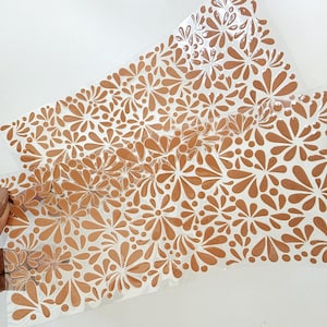 May include: Two sheets of clear, flexible material with a repeating floral pattern in a warm, earthy orange color. The design features stylized flowers and droplet shapes, creating a textured, decorative effect.