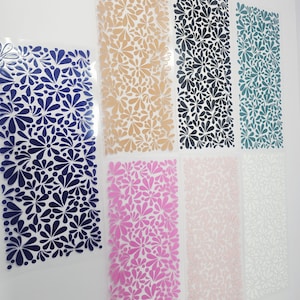 May include: A collection of floral pattern sheets in various colors, including navy blue, tan, black, teal, pink, light pink, and white. The sheets are arranged vertically, showcasing the repeating flower design. The background is a plain white surface.