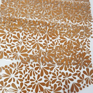 May include: Close-up of a sheet of brown floral stickers with a clear backing. The stickers feature a repeating pattern of stylized flowers and teardrop shapes. The stickers are arranged in rows and are partially peeled away from the backing.