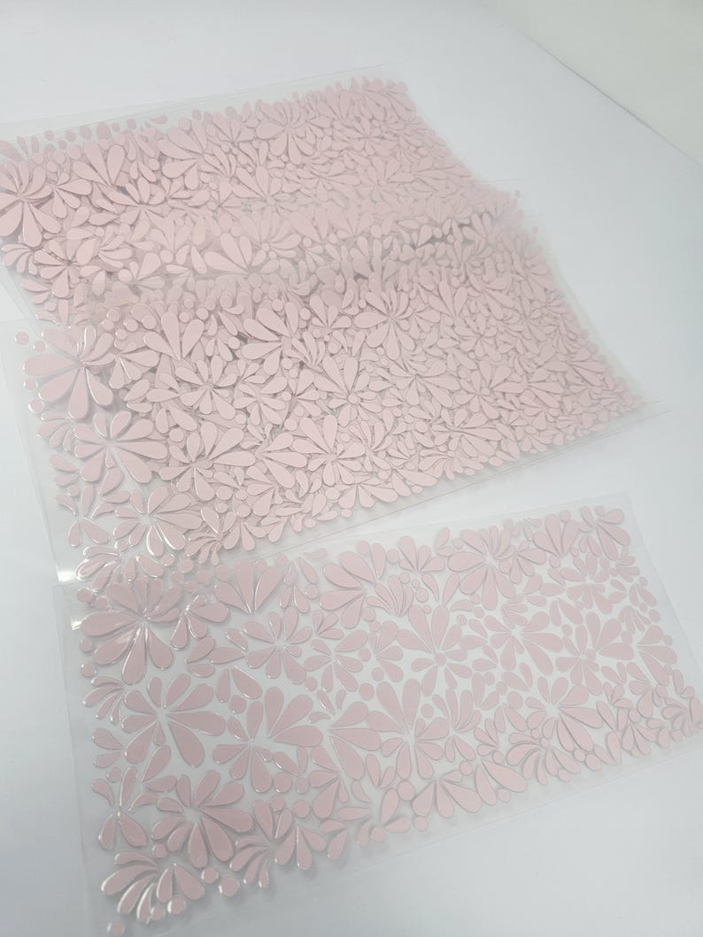 May include: Two sheets of pink floral patterned material. The sheets are transparent and the floral design is raised. The flowers are a soft pink color and cover the entire surface of the sheets. The sheets are laying on a white surface.