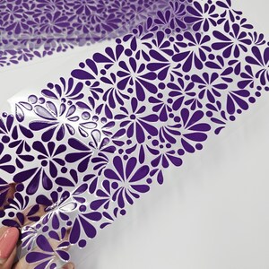 May include: Sheets of clear, flexible material with a repeating pattern of purple floral designs. The floral pattern is composed of stylized teardrop shapes and circular elements. The material is partially transparent, and the design is visible on the surface.