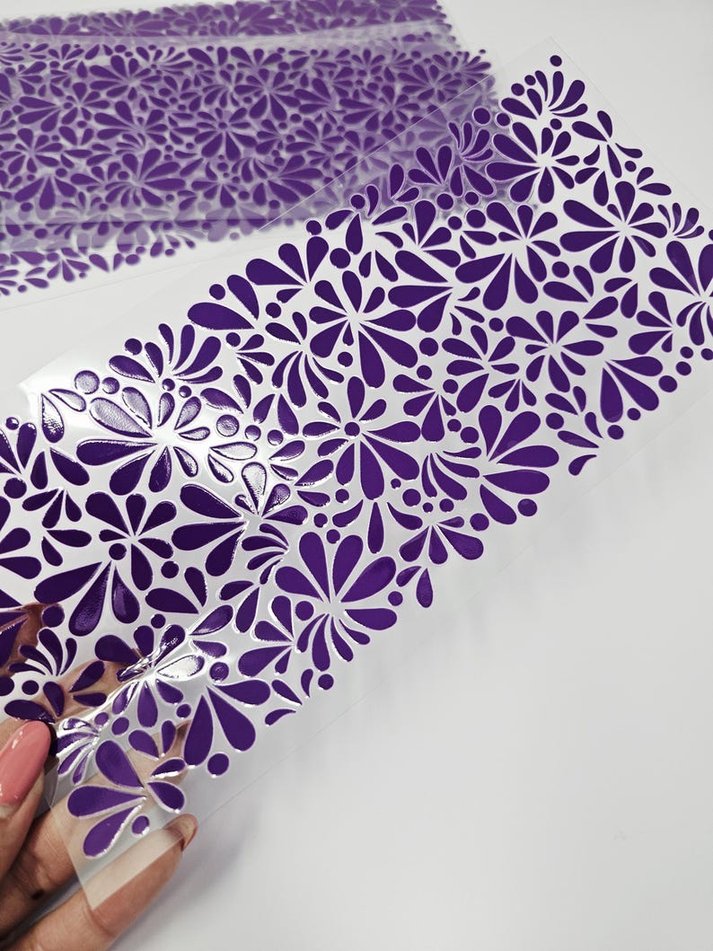 May include: Sheets of clear, flexible material with a repeating pattern of purple floral designs. The floral pattern is composed of stylized teardrop shapes and circular elements. The material is partially transparent, and the design is visible on the surface.