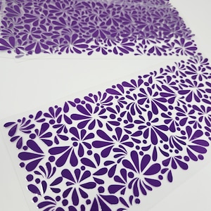 May include: Several sheets of clear plastic with a repeating pattern of purple floral shapes. The floral design is concentrated along the bottom edge of each sheet, creating a decorative border. The background is white.