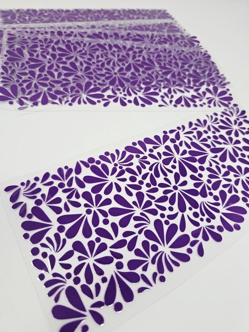 May include: Several sheets of clear plastic with a repeating pattern of purple floral shapes. The floral design is concentrated along the bottom edge of each sheet, creating a decorative border. The background is white.