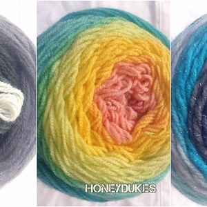 Op de afbeelding: Vijf kleurrijke garenbollen. De bollen zijn gelabeld met "MAGIC MOON", "HAPPY", "HONEYDUKES", "AQUARIUS (SPARKLE)" en "HERCULES". De garenkleuren zijn onder meer paars, grijs, blauw, geel, oranje en rood. Het garen is strak opgerold tot een bolvorm.