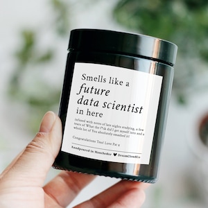 May include: A black candle jar with a white label that reads "Smells like a future data scientist in here infused with notes of late nights studying, a few tears of What the f*ck did I get myself into and a whole lot of You absolutely smashed it! Congratulations Tess! Love Pat x handpoured in Manchester DreamCloudCo"