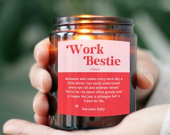 May include: A brown glass candle jar with a pink and red label that reads "Work Bestie (noun)". The label defines a work bestie as someone who makes every work day a little better.
