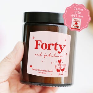 May include: A brown glass candle jar with a black lid. The label reads "Forty and fabulous" in red script. Additional text includes "Happy 40th birthday Carol! Love Erin x." A pink gift box tag is attached.