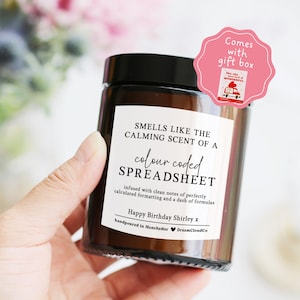 May include: A brown glass candle jar with a black lid, featuring a white label with the text "Smells Like The Calming Scent Of A Colour Coded Spreadsheet." A pink gift box sticker is attached. The candle is hand-poured in Manchester.