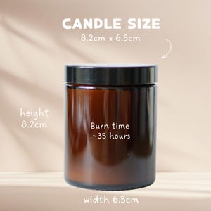 May include: A cylindrical amber glass candle jar with a black lid. Text on the jar reads: Burn time ~35 hours. Text above the jar reads: CANDLE SIZE 8.2cm x 6.5cm. Additional text indicates a height of 8.2cm and a width of 6.5cm.