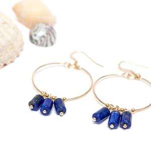 Könnte beinhalten: Goldene Creolen mit drei baumelnden Lapislazuli-Perlen.