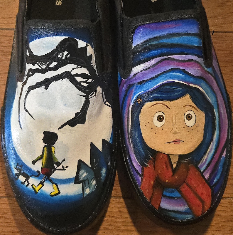 May include: Pair of black slip-on shoes, each painted with a different scene. One shoe features a silhouetted figure walking toward a house under a full moon. The other shoe depicts a girl with blue hair and a red scarf, surrounded by swirling colors.