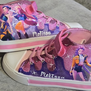 Może przedstawiać: Para wysokich trampek w odcieniach r&oacute;żu i fioletu z brokatowym wykończeniem. Buty posiadają nadrukowane postacie w stylu anime, białe gumowe noski, r&oacute;żowe sznurowadła oraz zapięcie na rzep. Imię Melissa jest namalowane białą czcionką.