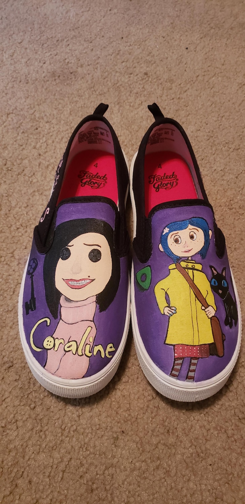 May include: Pair of custom-painted slip-on shoes featuring characters from the movie "Coraline." One shoe depicts Coraline with the text "Coraline," and the other shows Coraline in a yellow raincoat with a black cat. The shoes have purple uppers and white soles.