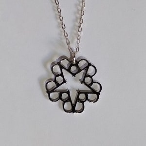 May include: A silver chain necklace with a silver star-shaped pendant. The star has a hollow center and is made of multiple interlocking circles.
