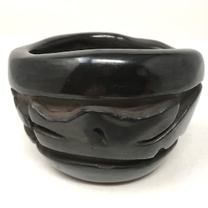 May include: Black pottery bowl with a carved design. The bowl is made of black clay and has a glossy finish.
