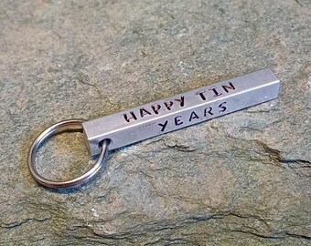 May include: A silver metal keychain with a rectangular bar that reads "Happy Tin Years".