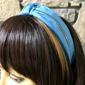 K&ouml;nnte beinhalten: Ein hellblaues Stirnband mit einem goldenen Rei&szlig;verschlussdetail. Das Stirnband ist aus einem weichen, dehnbaren Stoff gefertigt und perfekt, um jedem Outfit einen Hauch von Stil zu verleihen.