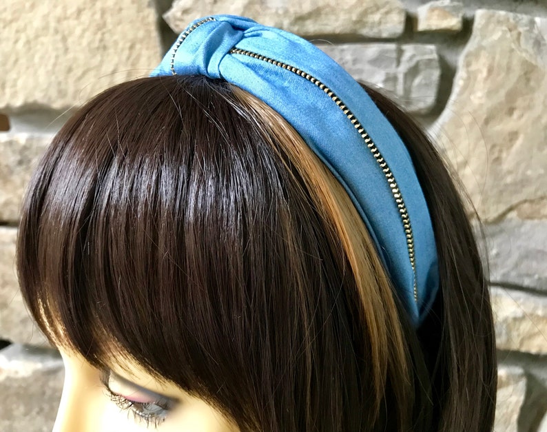 K&ouml;nnte beinhalten: Ein hellblaues Stirnband mit einem goldenen Rei&szlig;verschlussdetail. Das Stirnband ist aus einem weichen, dehnbaren Stoff gefertigt und perfekt, um jedem Outfit einen Hauch von Stil zu verleihen.