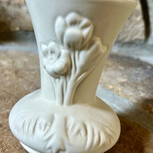 May include: Off-white ceramic vase with a flared top and a rounded base. The vase features embossed floral designs, including tulips. The vase is approximately 5 inches tall.