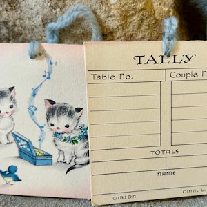 May include: Vintage Tally card with a charming illustration of two kittens with blue floral accents and a blue bird. The card has the word "TALLY" at the top and includes spaces for table and couple numbers.