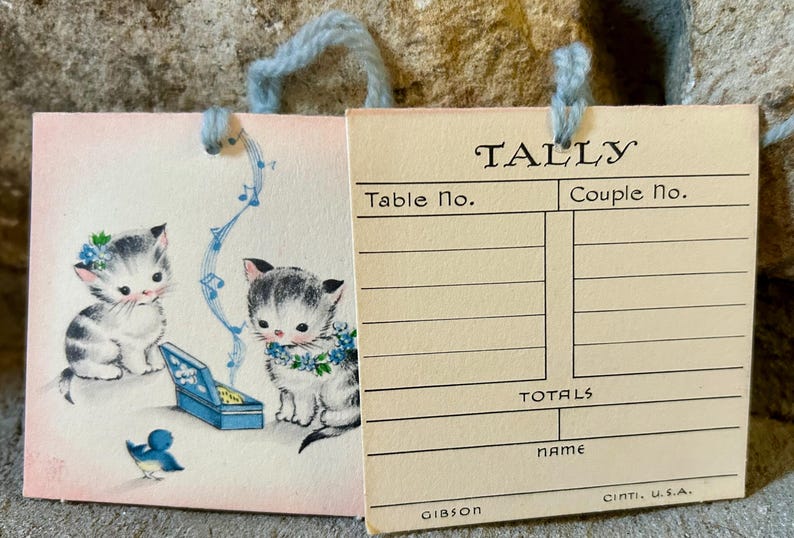 May include: Vintage Tally card with a charming illustration of two kittens with blue floral accents and a blue bird. The card has the word "TALLY" at the top and includes spaces for table and couple numbers.