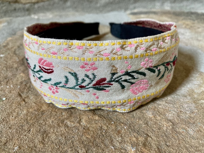 Op de afbeelding: Een beige hoofdband met een bloemenpatroon in roze, groen en bordeauxrood. De hoofdband heeft een gele rand.