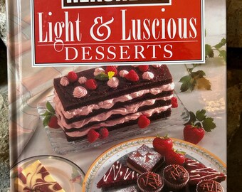 Może przedstawiać: Książka kucharska zatytułowana "HERSHEY'S Light & Luscious Desserts" przedstawiająca warstwowe ciasto czekoladowe z różowym lukrem i świeżymi truskawkami. Inne desery są wyświetlane na talerzach z tekstem "Every Recipe Low in Fat, Calories & Cholesterol".