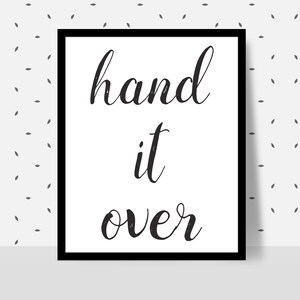 May include: A framed print with the words "hand it over" in a stylish, cursive font. The text is in black against a white background, framed by a black border. The background has a subtle pattern of small, gray leaf shapes.