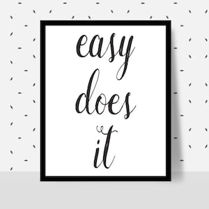 Puede incluir: Un cuadro enmarcado con la frase "easy does it" en escritura negra sobre un fondo blanco. El marco es negro y el fondo tiene un patrón de pequeñas formas de hojas grises.