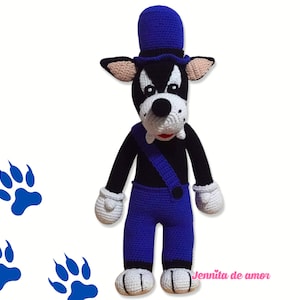 Puede incluir: Un perro de peluche de crochet que lleva un sombrero azul y un mono. El perro tiene pelo negro, patas blancas y una boca roja. El perro está de pie sobre un fondo blanco con tres huellas de patas azules.