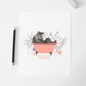 Puede incluir: Un oso negro sentado en una ba&ntilde;era rosa con lunares blancos. El oso est&aacute; rodeado de plantas verdes en macetas.