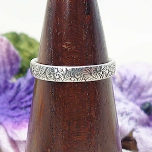 Peut inclure: Une bague en argent avec un motif floral complexe. La bague est présentée sur un porte-bague en bois.