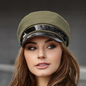 May include: A green and black cap with a wide brim and a shiny black band. The cap has a button on the side.