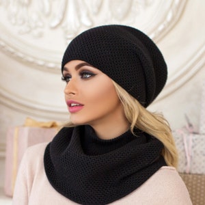 May include: Black knitted beanie and matching infinity scarf. The beanie has a slouchy fit and the scarf is made from a thick, cosy fabric.
