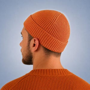 May include: A vibrant orange beanie with a thick, ribbed knit texture and a folded cuff. The hat features a vertical ribbed pattern that extends from the crown to the edge of the cuff, providing a consistent, textured appearance throughout the design.