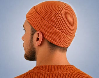 May include: A vibrant orange beanie with a thick, ribbed knit texture and a folded cuff. The hat features a vertical ribbed pattern that extends from the crown to the edge of the cuff, providing a consistent, textured appearance throughout the design.